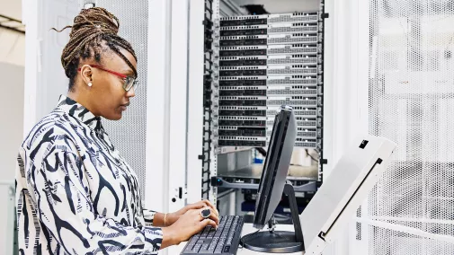 Eine Frau sitzt am Computer und arbeitet am Server.