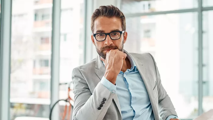 man with glasses sits thoughtfully in office