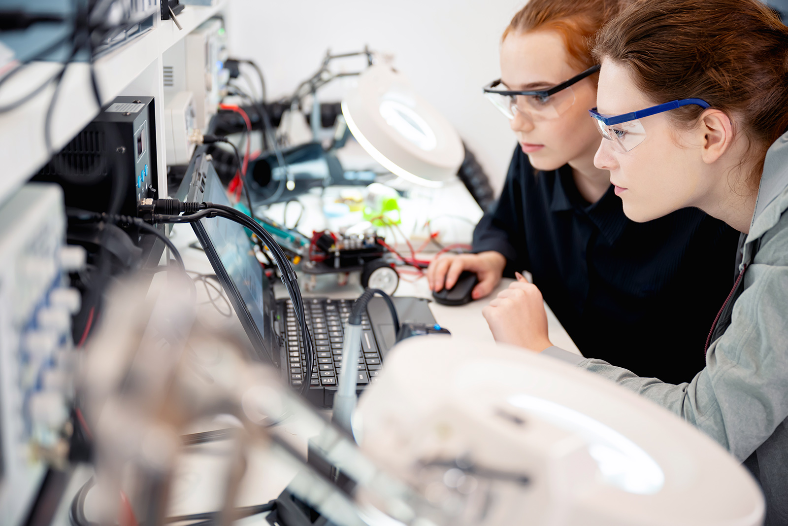 Two women working on electronics at a desk.
