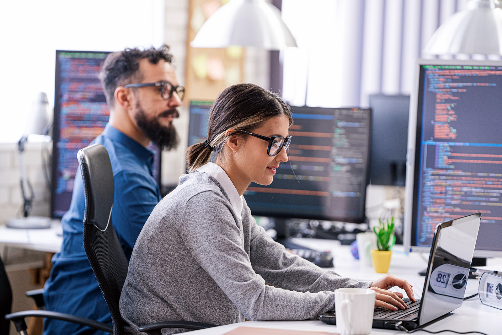 Two people are programming something on a laptop.