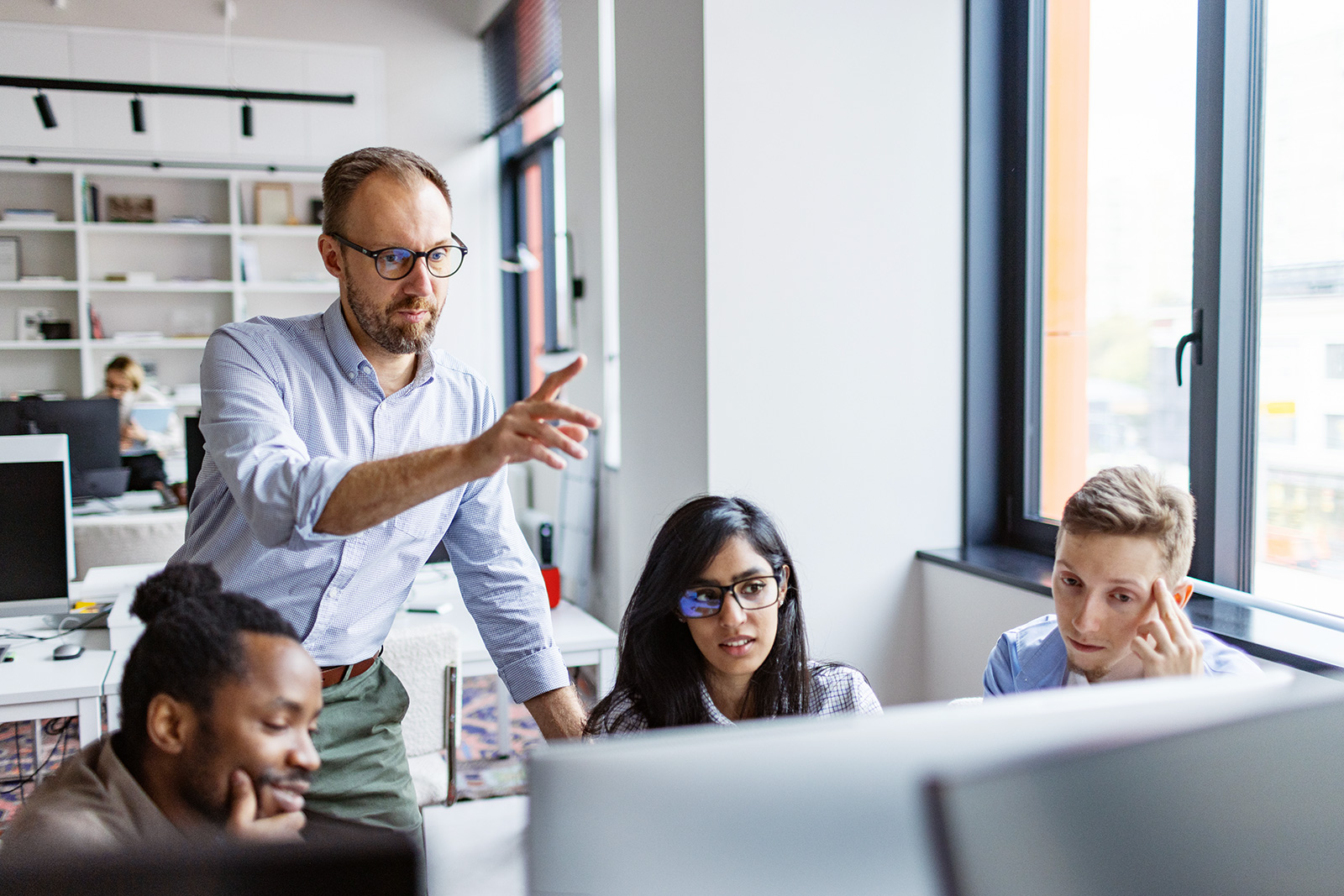 Three people are sitting in front of a computer in a meeting.