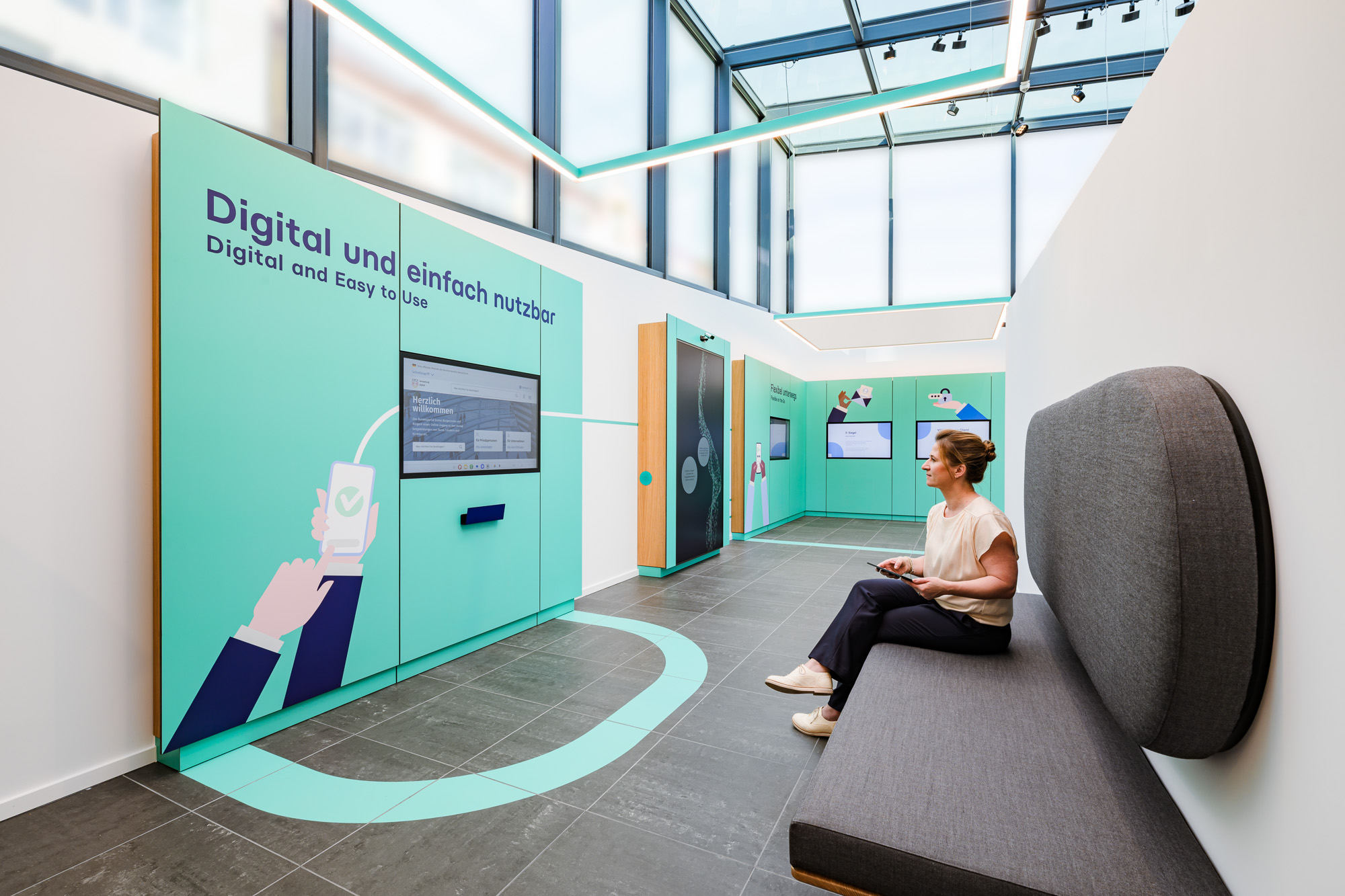 Frau sitzt auf Couch und schaut sich im Showpavillon Exponate der digitalen Verwaltung an