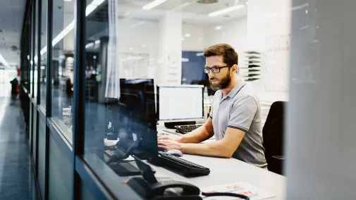 Ein Mann sitzt im Büro am Schreibtisch und arbeitet am Computer