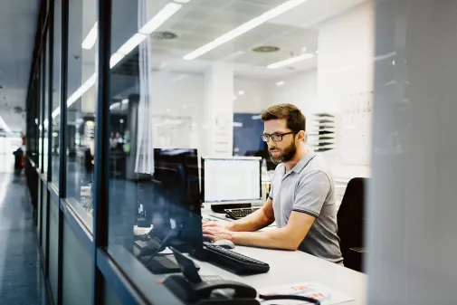 Ein Mann sitzt im Büro am Schreibtisch und arbeitet am Computer