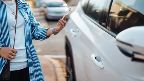Person schaut aufs Handy vor dem Auto