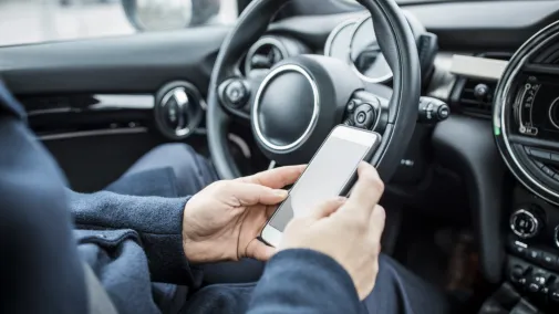 Person sitzt im Auto und schaut aufs Handy