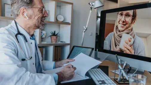 Arzt sitzt am Schreibtisch im Gespräch mit Patientin