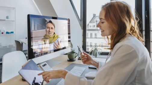 Ärztin telefoniert mit Patient am Computer in der Praxis.