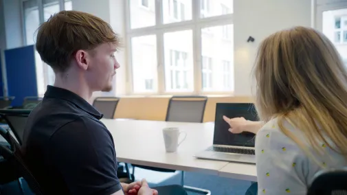 Two people are sitting in front of a computer and talking.