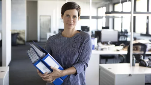 Frau steht mit Akten im Arm im Büro Frau steht mit Akten im Arm im Büro