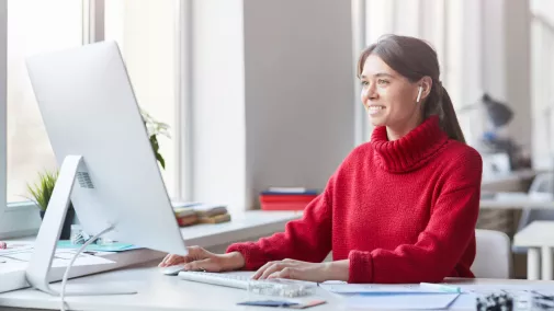 Frau mit Kopfhörern sitzt am Computer am Tisch im Büro Frau mit Kopfhörern sitzt am Computer am Tisch im Büro
