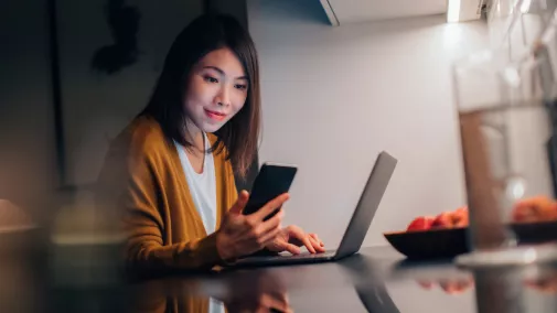 women with smartphone sitting on computer at home