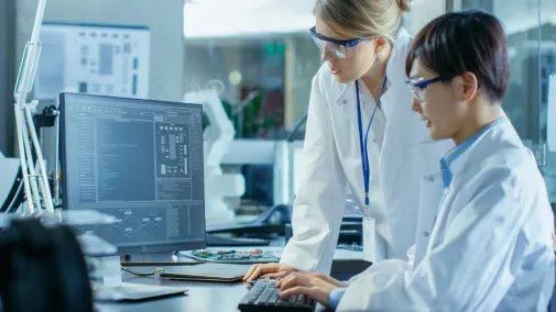 Zwei Frauen sitzen im Labor am Computer und forschen .