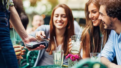 Frauen und Männer zahlen mit Smartphone trinken am Tisch im Cafe draussen