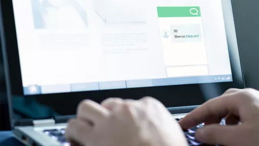 Detailaufnahme eines Laptop-Bildschirms, auf dem ein Chatbot abgebildet es. Man sieht, wie männliche Hände etwas tippen und mit dem Chatbot interagieren.