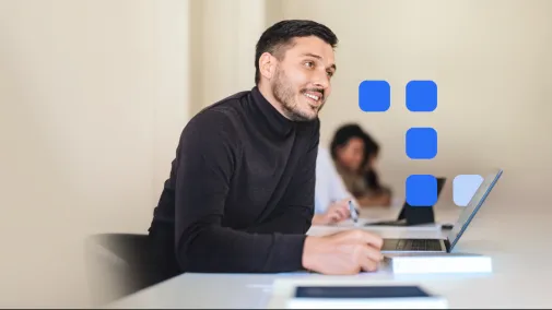 A man sits at his desk in front of his laptop and writes something down. 