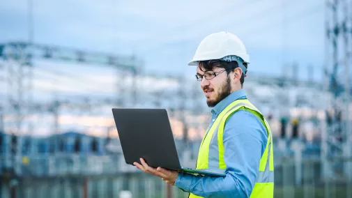 mann with helmet and safety vest looks into computer