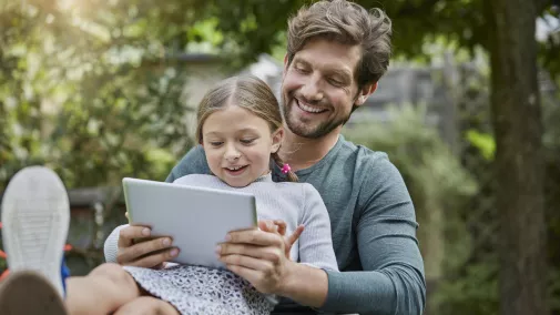Mann und Kind sitzen mit Tablet draussen Mann und Kind sitzen mit Tablet draussen