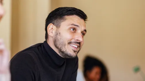 Mann sitzt am Schreibtisch vor dem Laptop und schreibt sich etwas auf. 