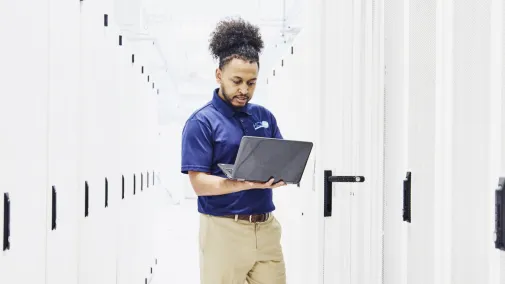 Mann mit Notebook steht im Serverraum Mann mit Notebook steht im Serverraum