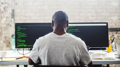 Foto eines Mannes, der vor einem Computer sitzt und programmiert