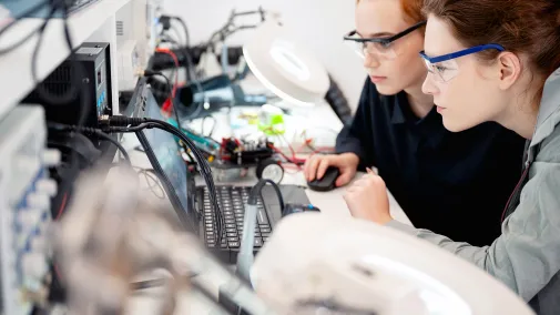 Two women working on electronics at a desk.