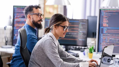 Two people are programming something on a laptop.