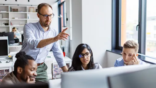 Drei Personen sitzen im Meeting vor einem Computer.