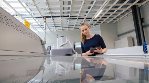 The image shows a woman in front of the printing press, operating it.