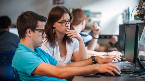View of two people sitting in front of a computer.