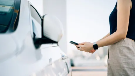 Frau mit Smartphone stehend am Auto 