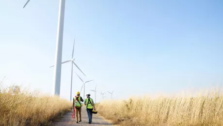 zwei Männer laufen über ein Feld umgeben von Windrädern