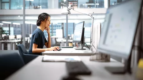 Frau sitzt am Arbeitsplatz vor einem Computer.
