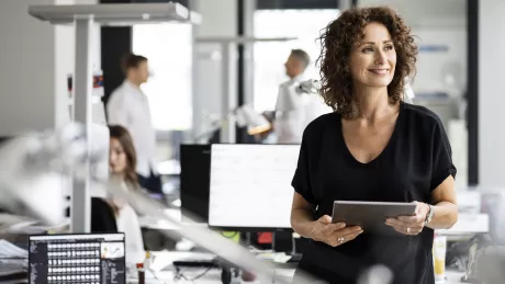 Frau mit Tablet lehnt an Schreibtisch