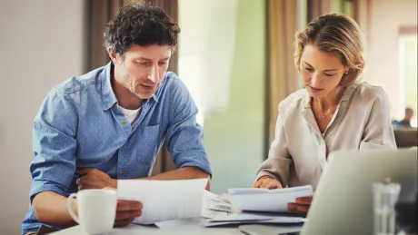 Frau und Mann mit Zettel und Notebook am Tisch zu Hause