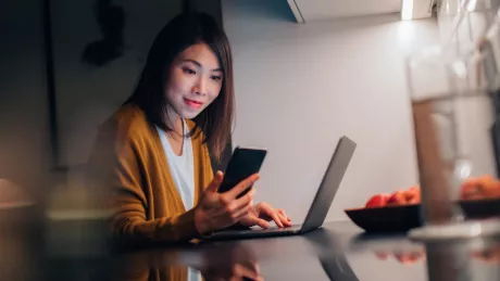 women with smartphone sitting on computer at home