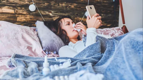 Frau mit Smartphone liegt krank im Bett