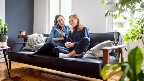 women sitting on a couch with smartphone laughing at home
