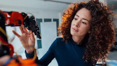 Foto einer jungen Frau, die einen Roboterarm betrachtet und mit den Fingern berührt