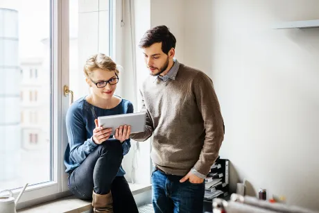 A man and a woman are viewing a website on a tablet.
