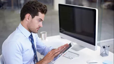 Mann arbeit mit Tablet und Computer am Schreibtisch