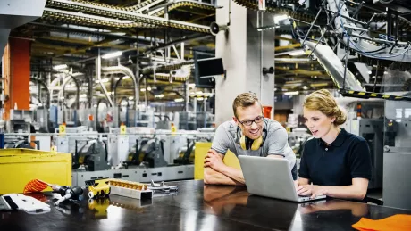 Mann und Frau stehen an einem Laptop in einer Industriehalle