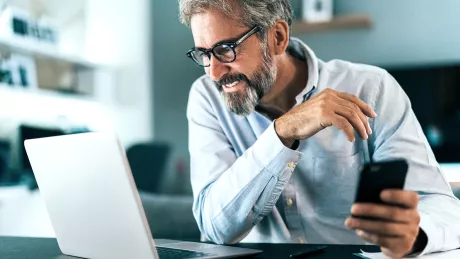 Mann sitz mit Smartphone vor einem Laptop 