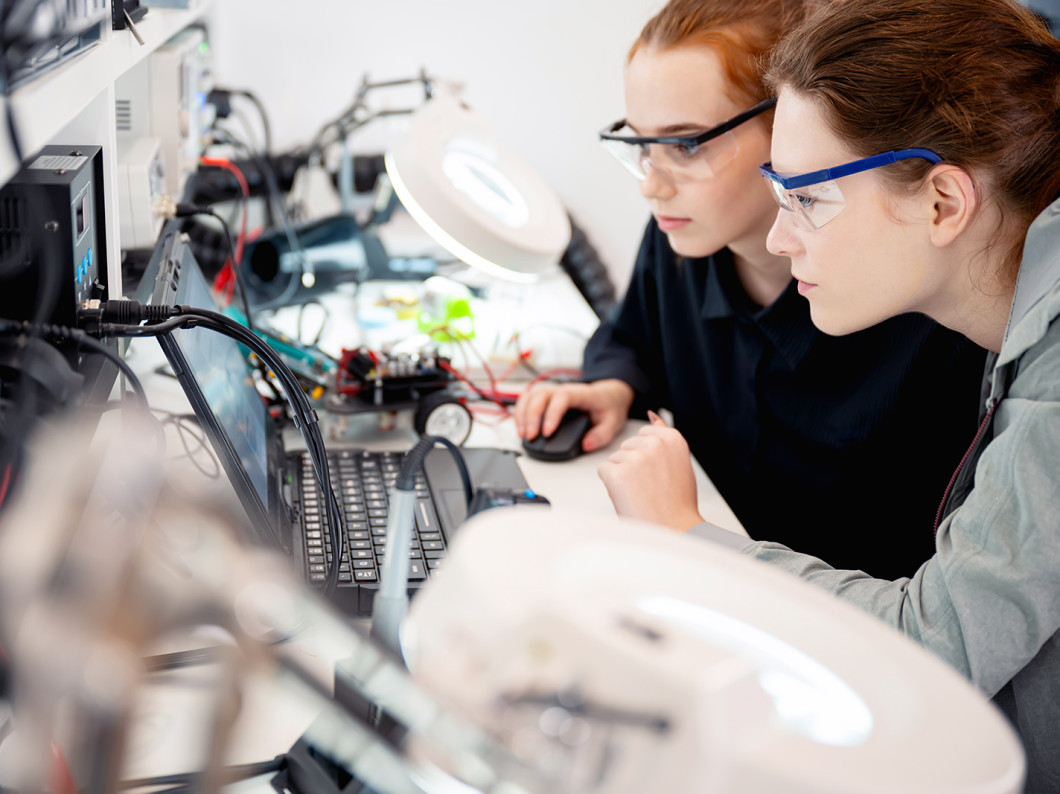 Two women working on electronics at a desk.