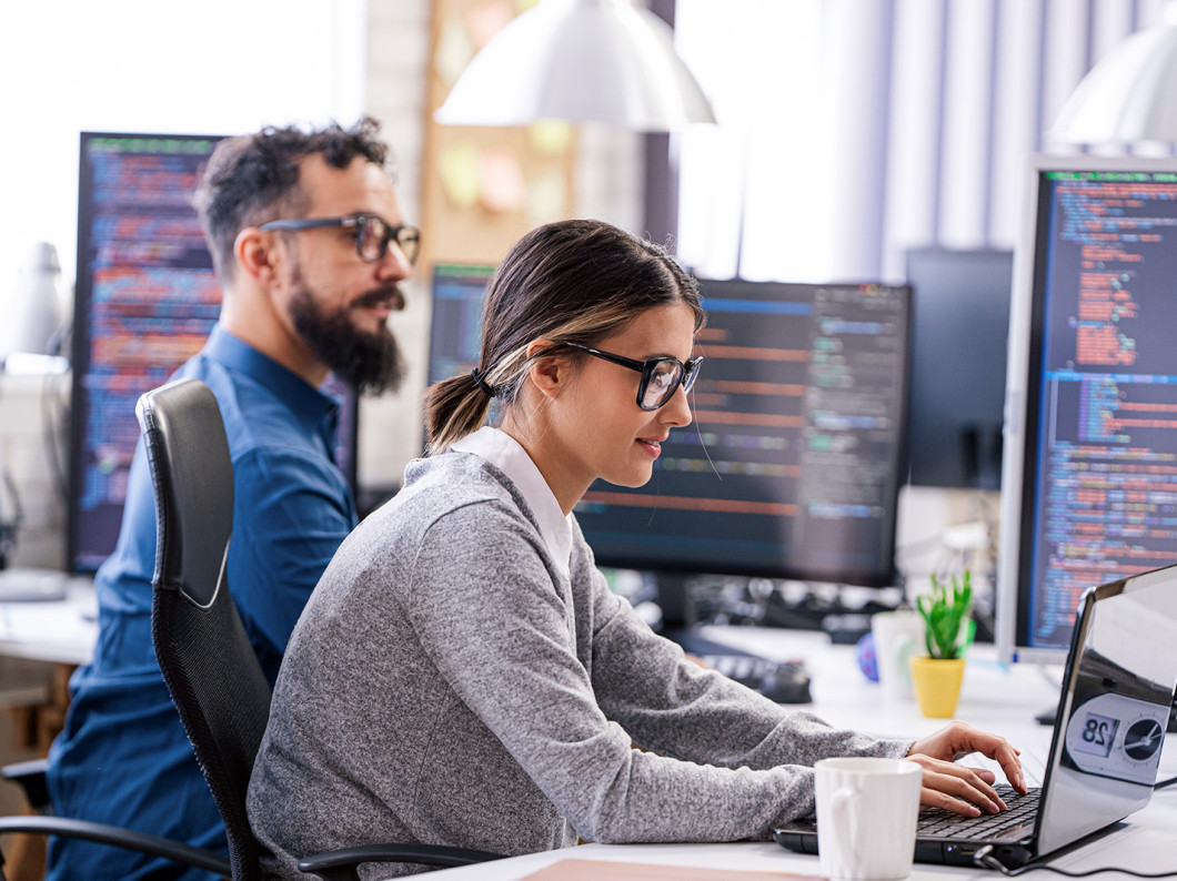 Two people are programming something on a laptop.