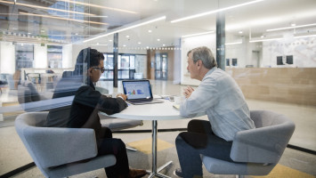 Personen sitzen am Tisch mit einem Laptop