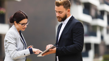 A woman and a man digitally signing on a tablet outdoors.