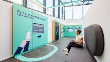 Frau sitzt auf Couch und schaut sich im Showpavillon Exponate der digitalen Verwaltung an