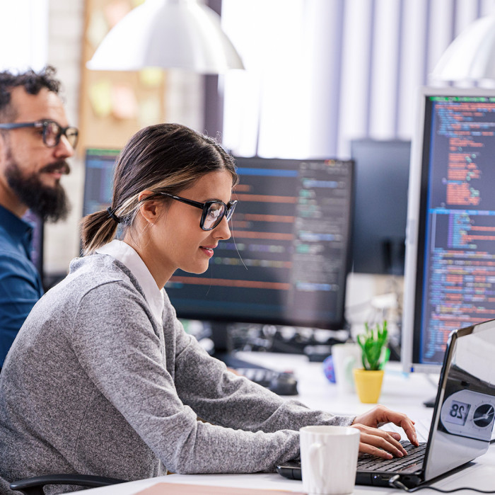 Two people are programming something on a laptop.