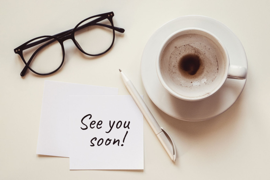 Ein Tisch mit einer Brille, Tasse Kaffee und einem Notizzettel "see you soon"
